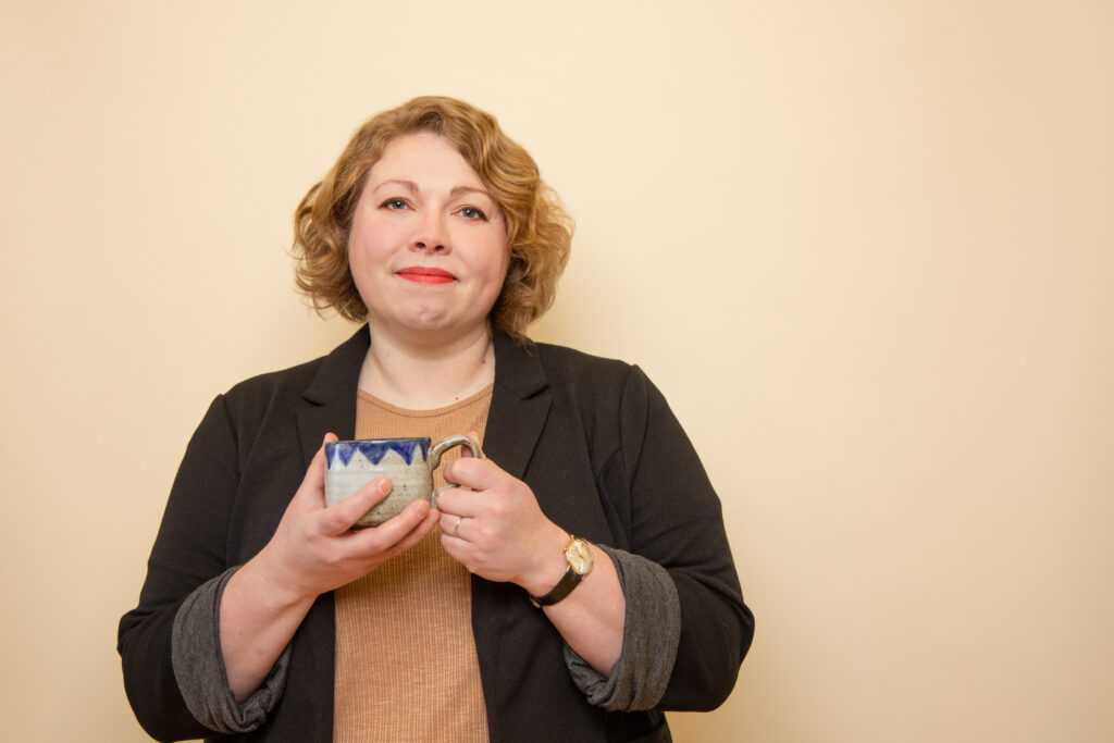 Sarah Shapiro looking at the camera with a slight smile, holding a ceramic mug.